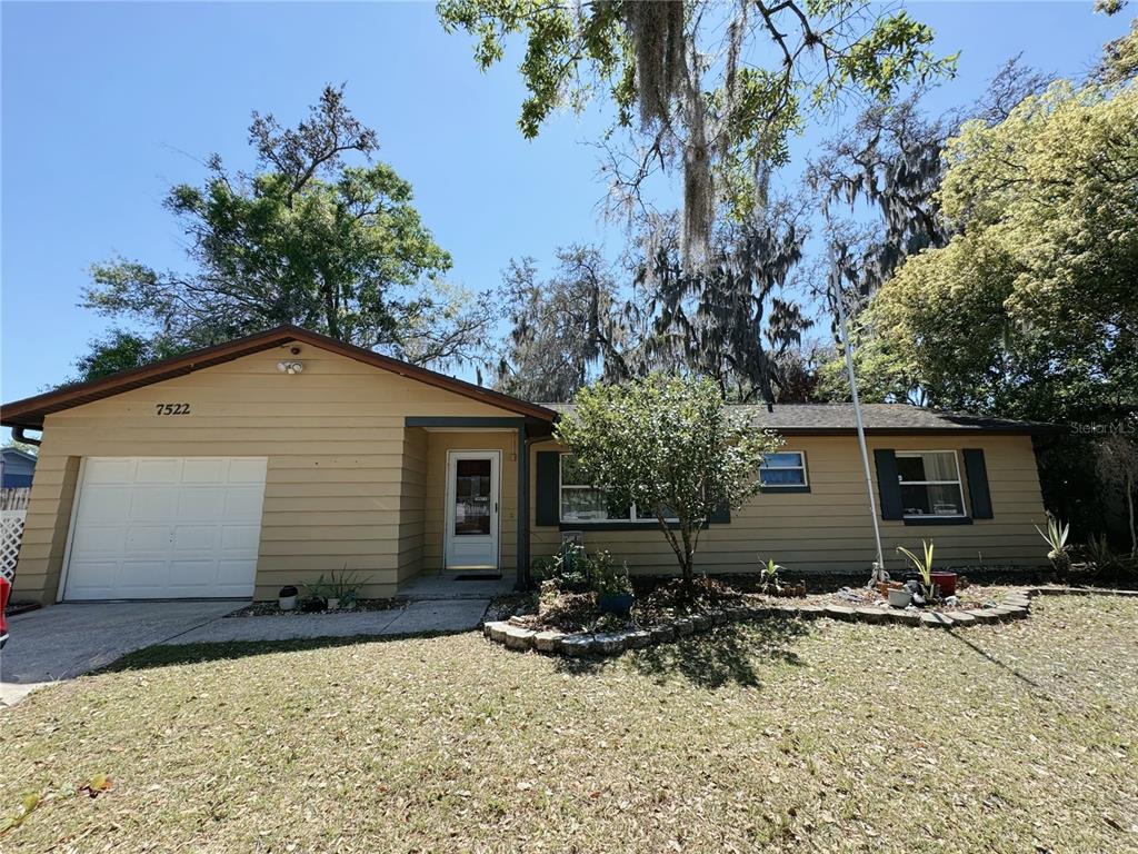 A single-story house with tan siding, a white garage door, and a front yard — 7522 LAUREL SPRINGS DRIVE, WINTER PARK, FL