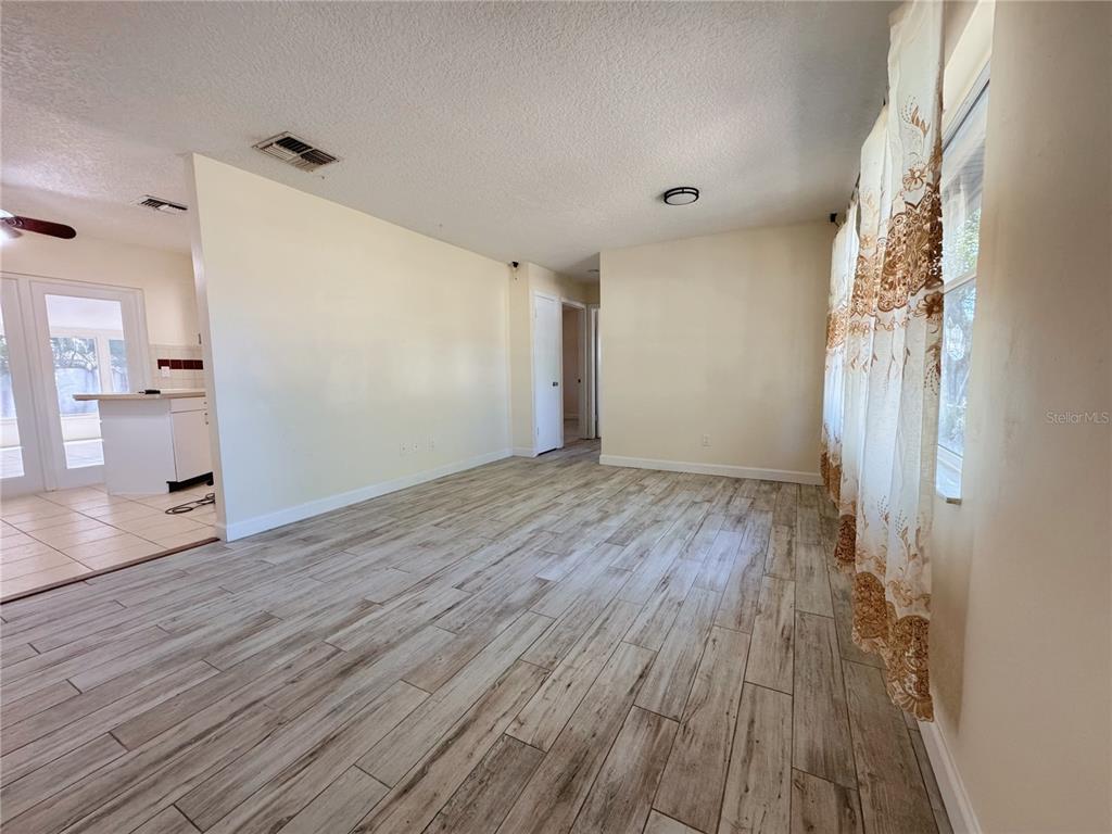 A living room with light-colored walls, wood-look tile flooring, and a view into the kitchen — 7522 LAUREL SPRINGS DRIVE, WINTER PARK, FL