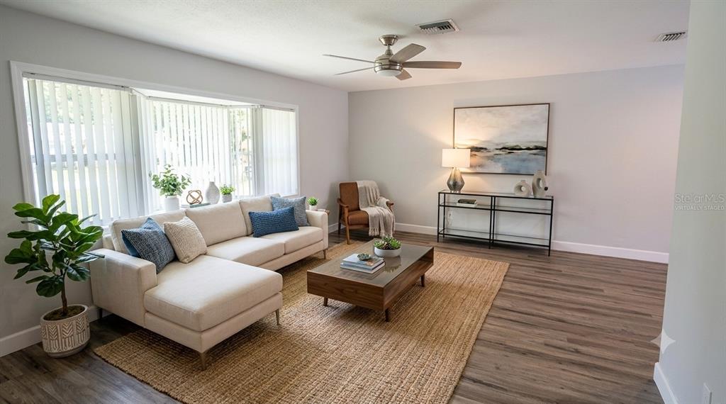 A living room features a stone fireplace, a beige sectional sofa, and wood-look flooring — 7801 17TH WAY N, ST PETERSBURG, FL