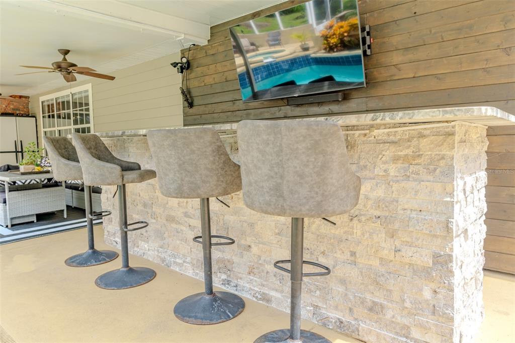 An outdoor bar with stone veneer, gray stools, and a television mounted on wood paneling — 33721 SPRING DRIVE, LEESBURG, FL