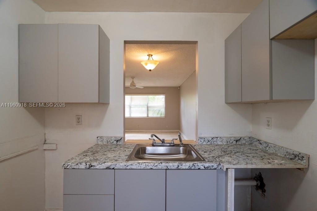 A kitchen sink with granite countertops and gray cabinets overlooks an adjacent living area — 550 SE 2nd Ave # G25, Deerfield Beach FL 33441, DEERFIELD BEACH, FL