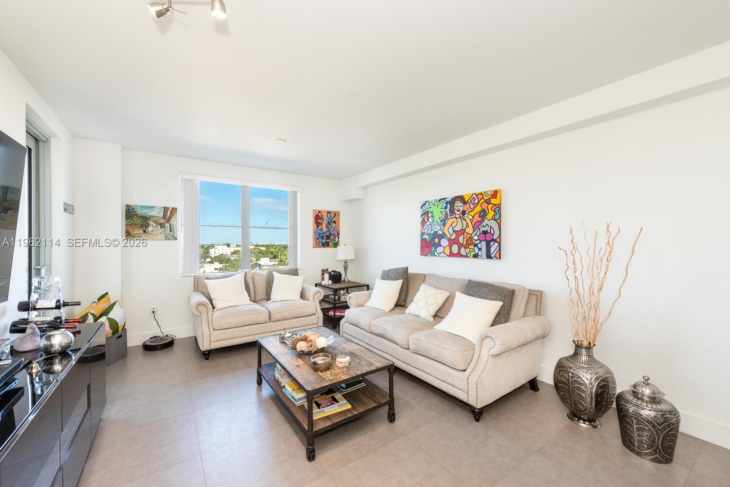A living room features light-colored sofas, a wooden coffee table, and colorful wall art — 1830 Radius Dr # 709, Hollywood FL 33020, HOLLYWOOD, FL