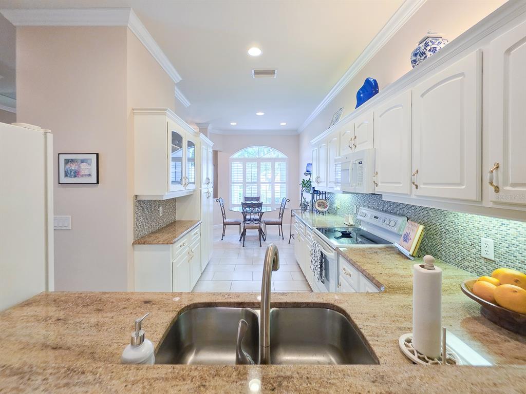 A kitchen features white cabinets, granite countertops, a double sink, and a dining area beyond — 3137 KAILANI COURT, ORMOND BEACH, FL