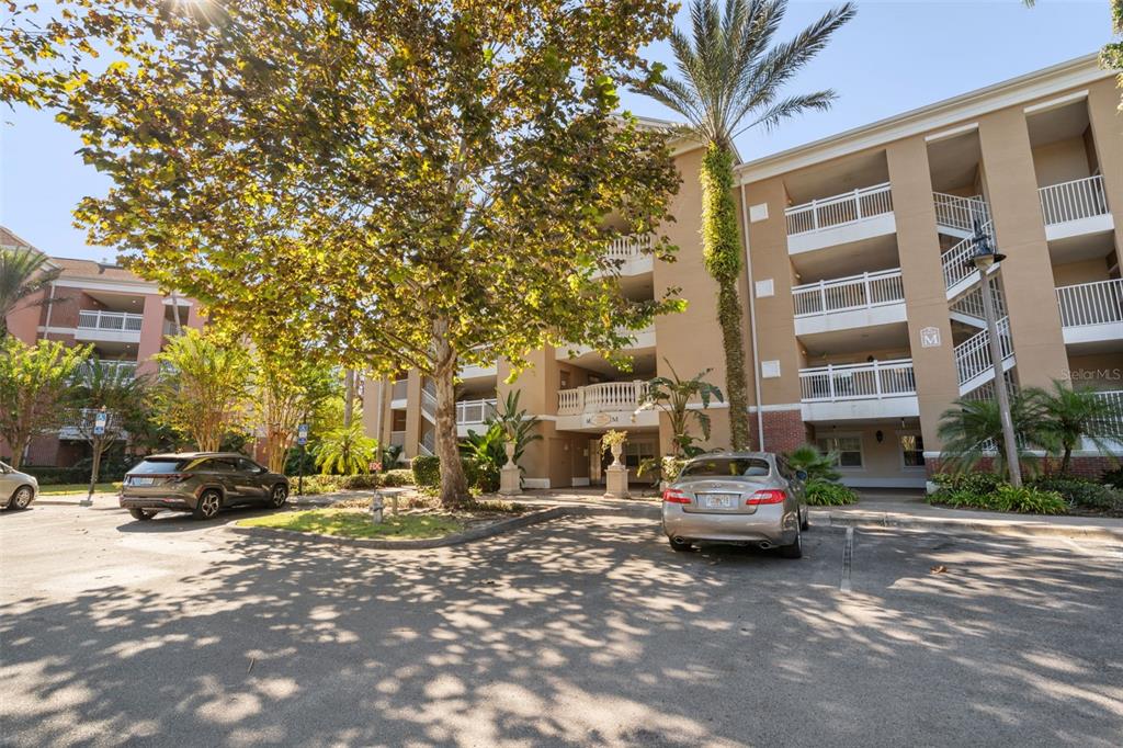 A multi-story apartment building with tan stucco walls and white balconies sits behind a parking lot — 7658 WHISPER WAY UNIT 202, REUNION, FL