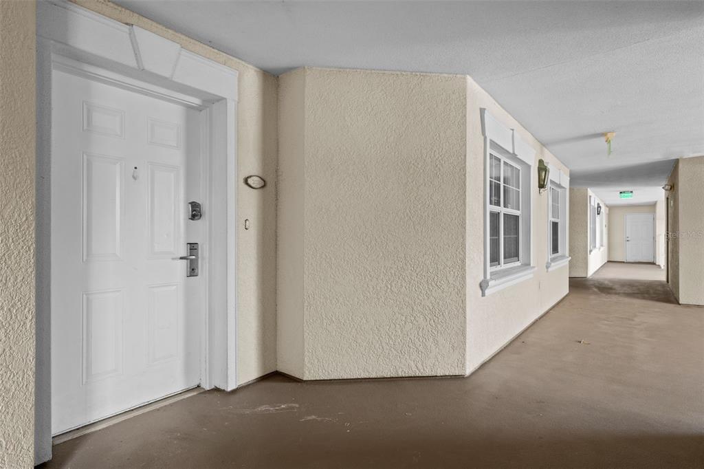 A covered outdoor walkway leads to a white front door with a textured beige wall — 7658 WHISPER WAY UNIT 202, REUNION, FL
