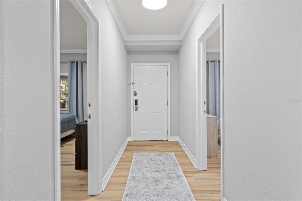 A hallway with light wood flooring, a runner rug, and a white door at the end — 7658 WHISPER WAY UNIT 202, REUNION, FL