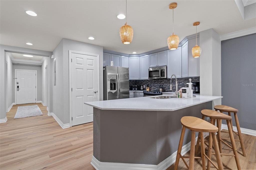 A kitchen features light blue cabinets, a white countertop, and three wooden bar stools — 7658 WHISPER WAY UNIT 202, REUNION, FL