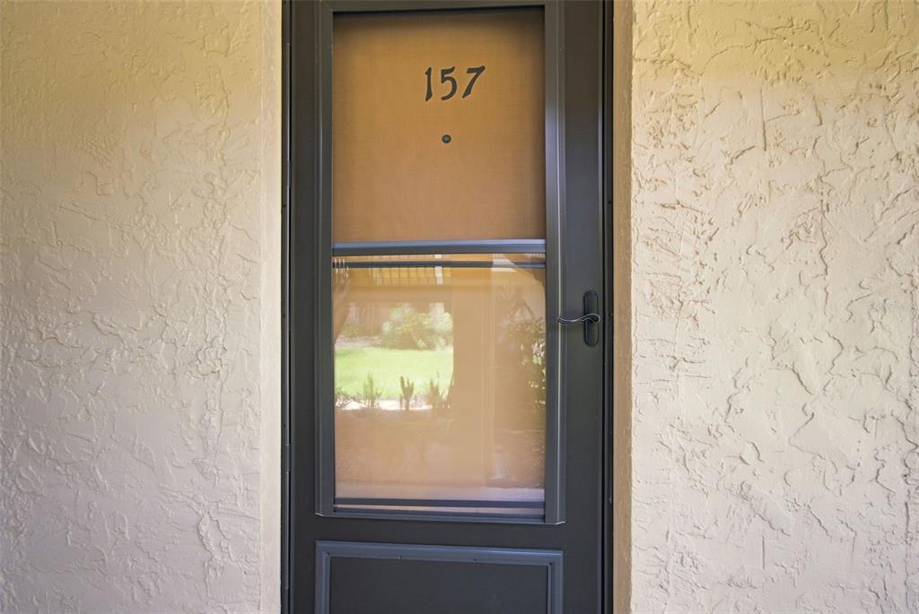 A dark-framed storm door with the number 157 is mounted on a textured beige wall — 8931 BLIND PASS ROAD UNIT 157, ST PETE BEACH, FL
