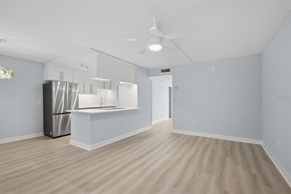 A kitchen with white cabinets and stainless steel appliances opens into a light-walled living area — 8931 BLIND PASS ROAD UNIT 157, ST PETE BEACH, FL