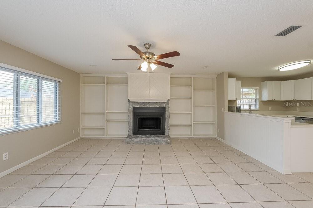 A living room features a stone fireplace, built-in shelving, tile flooring, and a ceiling fan — 15709 SQUIRREL TREE PLACE, TAMPA, FL