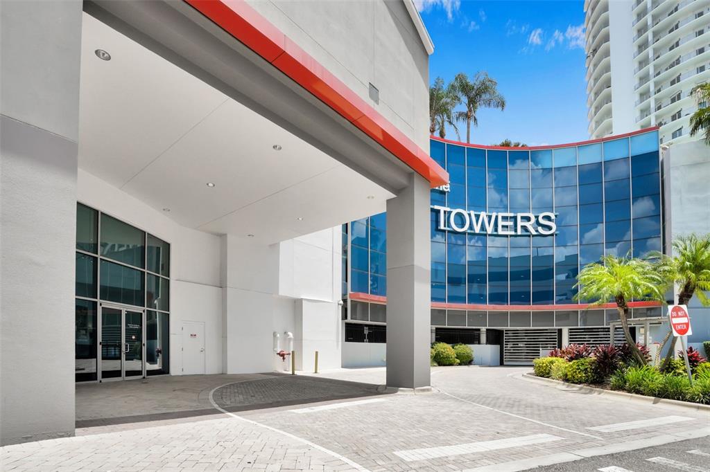 A paved driveway leads to a building entrance with a white overhang and glass facade — 1209 E CUMBERLAND AVENUE UNIT 2601, TAMPA, FL