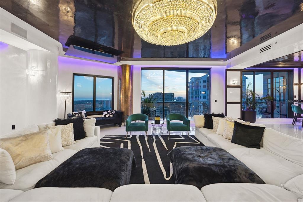 A modern living room features a large crystal chandelier, reflective ceiling, and floor-to-ceiling windows — 1209 E CUMBERLAND AVENUE UNIT 2601, TAMPA, FL