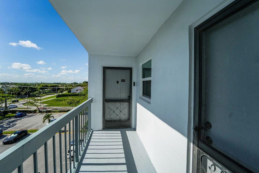 An exterior balcony with a metal railing overlooks a parking lot and green space — 6500 NW 2nd Avenue # 509, Boca Raton FL 33487, BOCA RATON, FL