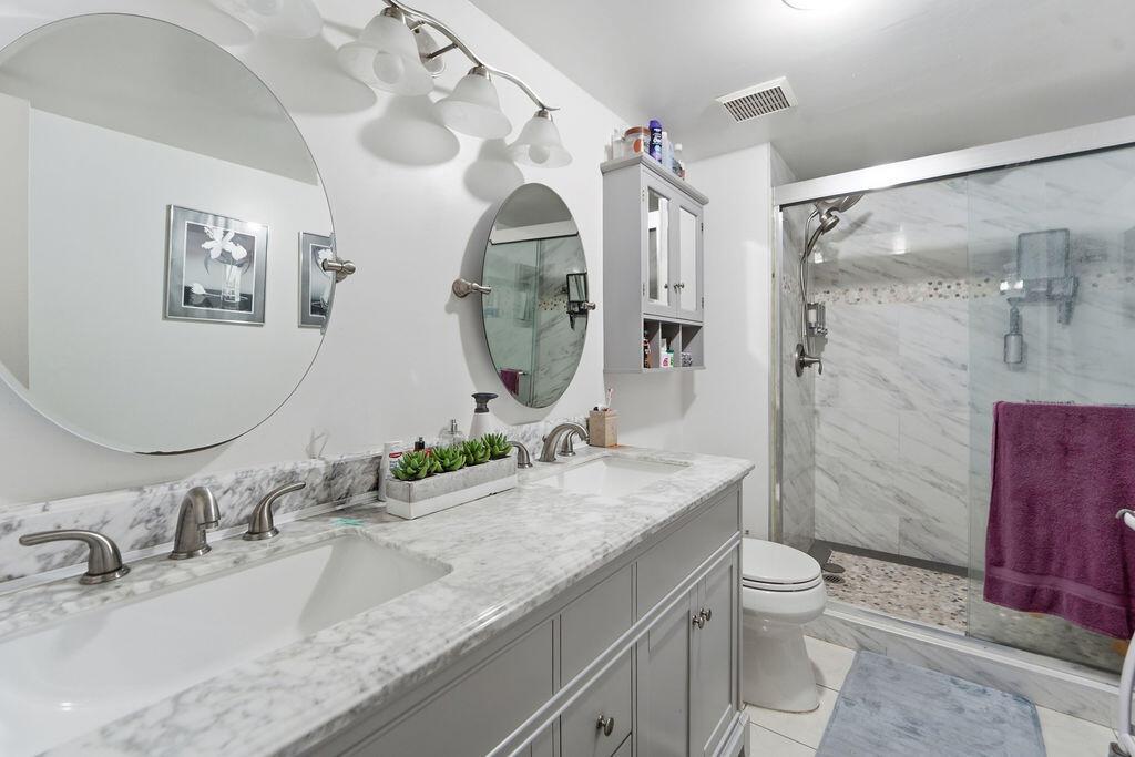 A bathroom features a double vanity with a marble countertop, gray cabinets, and a glass shower — 6500 NW 2nd Avenue # 509, Boca Raton FL 33487, BOCA RATON, FL