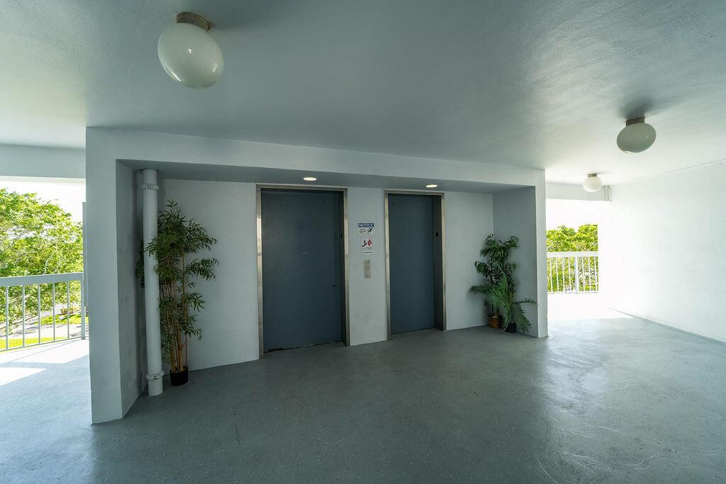 An outdoor elevator lobby with two gray doors, potted plants, and white concrete walls — 6500 NW 2nd Avenue # 509, Boca Raton FL 33487, BOCA RATON, FL
