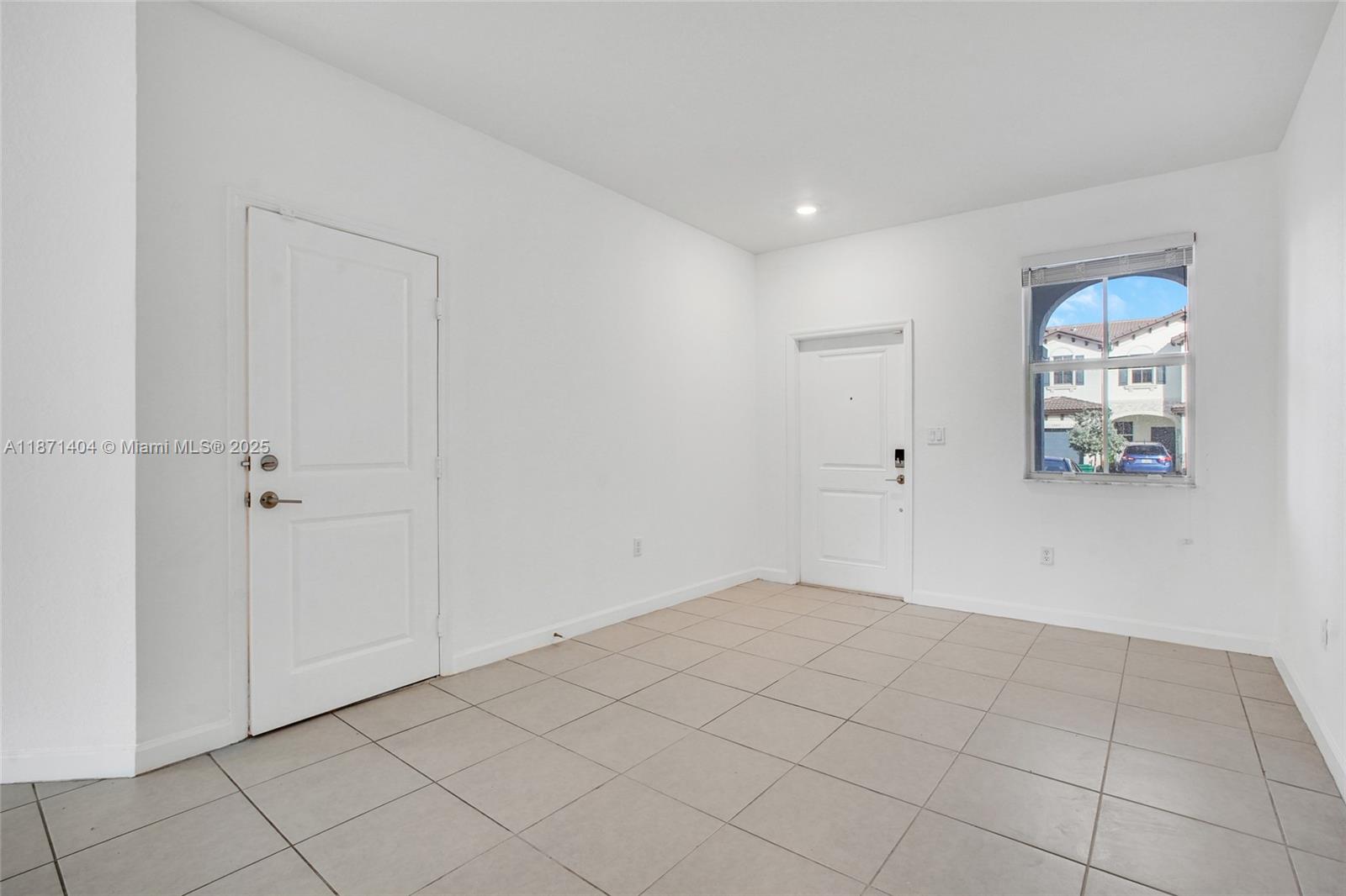 An empty room features white walls, light-colored tile flooring, two white doors, and a window — 12609 NW 23rd Pl, Miami FL 33167, MIAMI, FL