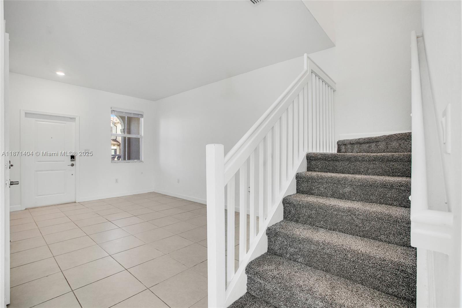 A room with tiled flooring, a white door, a window, and carpeted stairs — 12609 NW 23rd Pl, Miami FL 33167, MIAMI, FL