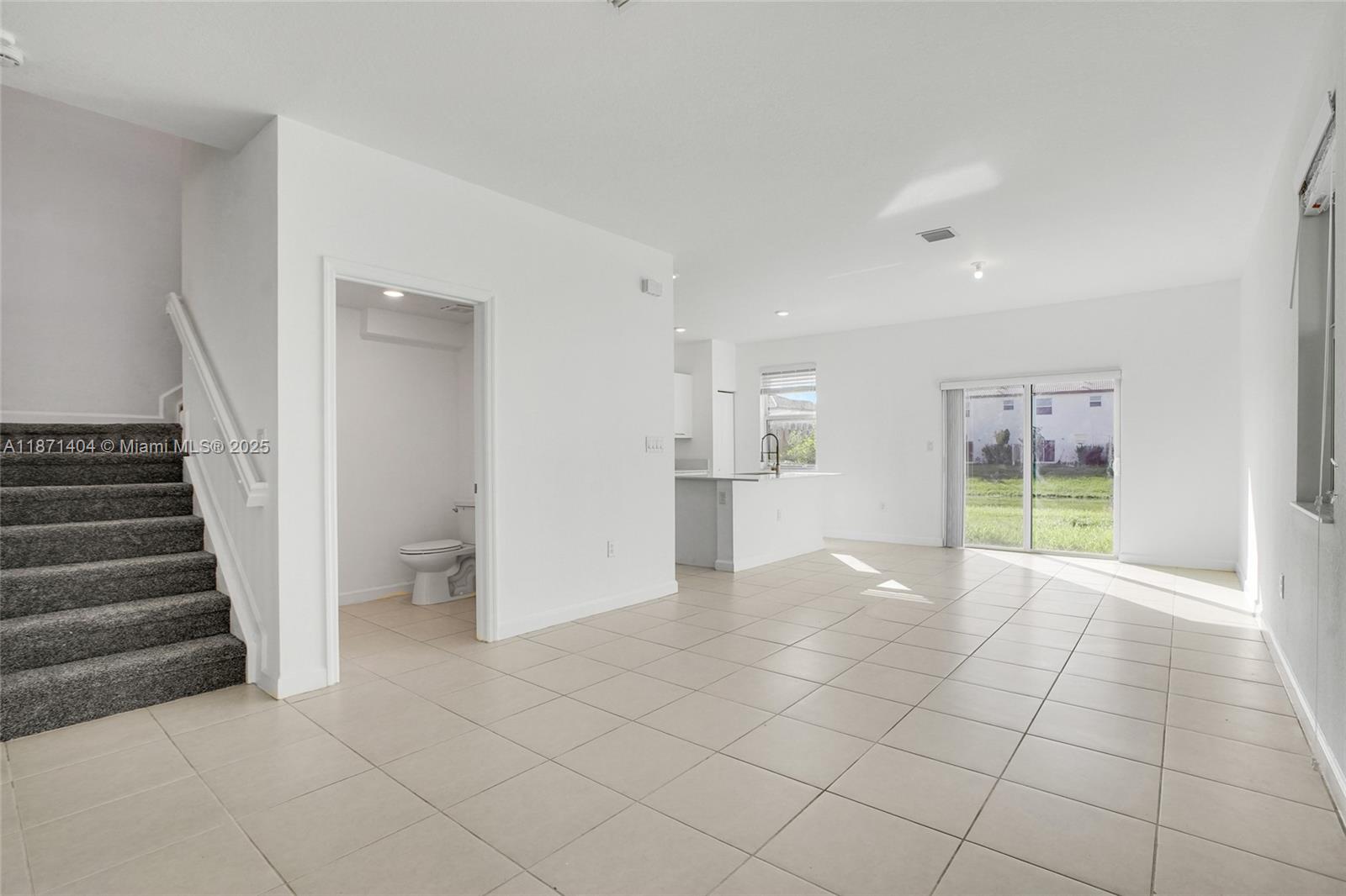 An open-concept living area features tile flooring, a carpeted staircase, and an adjacent half bathroom — 12609 NW 23rd Pl, Miami FL 33167, MIAMI, FL