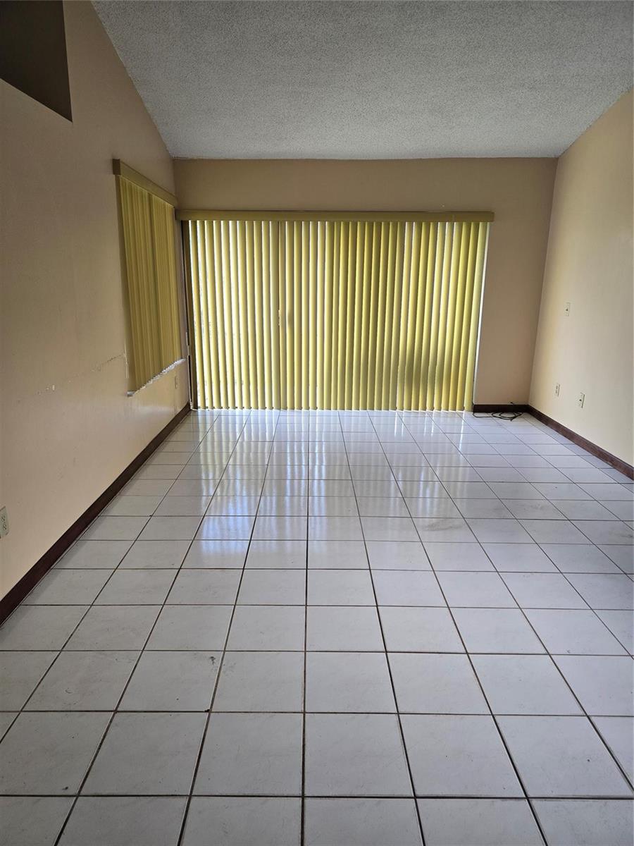 An empty room features white tile flooring, beige walls, and floor-to-ceiling vertical blinds — 12730 SW 112th Street, Miami FL 33186, MIAMI, FL