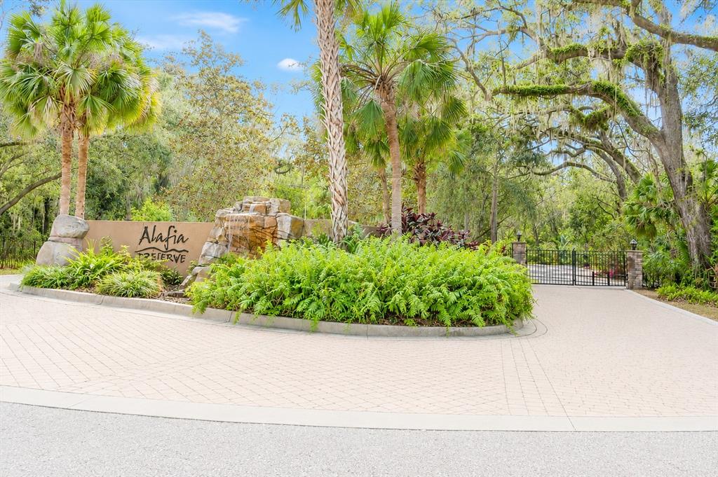 The entrance to Alafia Preserve features a stone waterfall, lush landscaping, and a gated driveway — 4876 RAMBLING RIVER ROAD, BRANDON, FL