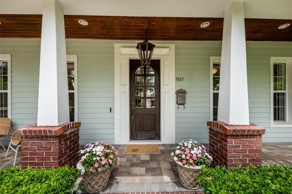 The front porch features a dark wood door, brick-based columns, and potted flowers — 1581 MAGNOLIA AVE, WINTER PARK, FL