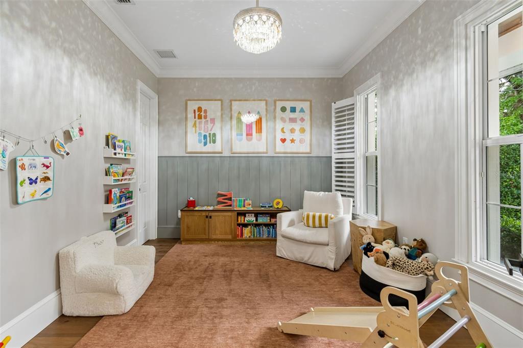 A playroom features a wooden storage unit, a white armchair, a rug, and wall art — 1581 MAGNOLIA AVE, WINTER PARK, FL