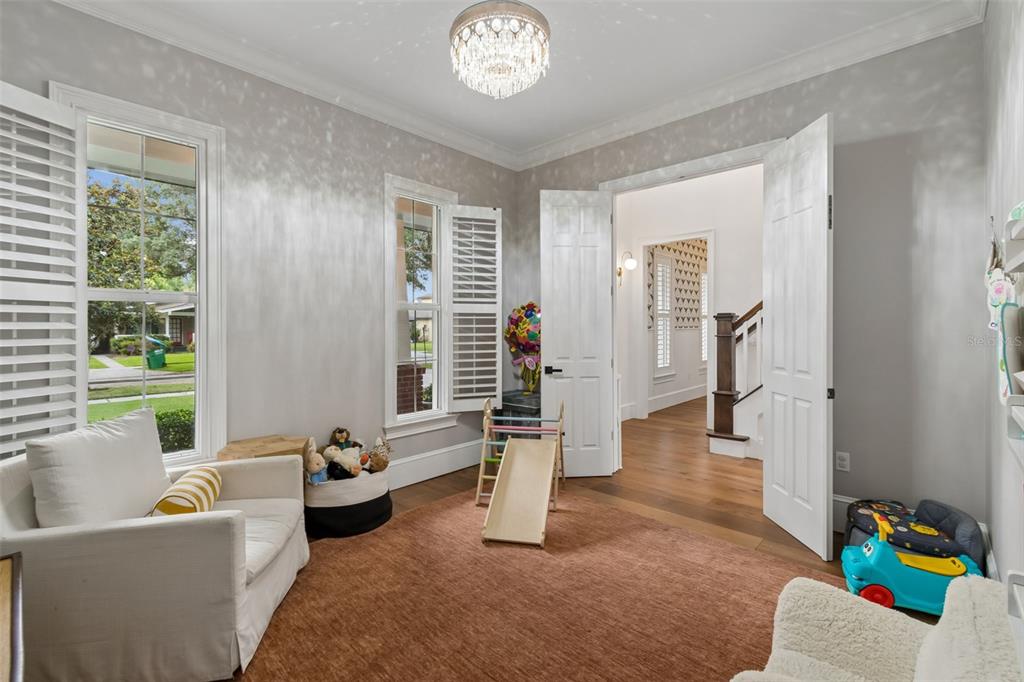 A playroom features a crystal chandelier, white plantation shutters, and double doors leading to a hallway — 1581 MAGNOLIA AVE, WINTER PARK, FL