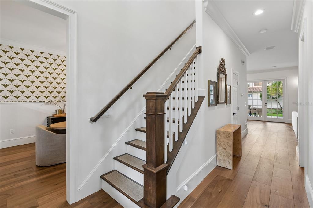 A staircase with a wooden handrail and white balusters sits in a bright hallway — 1581 MAGNOLIA AVE, WINTER PARK, FL