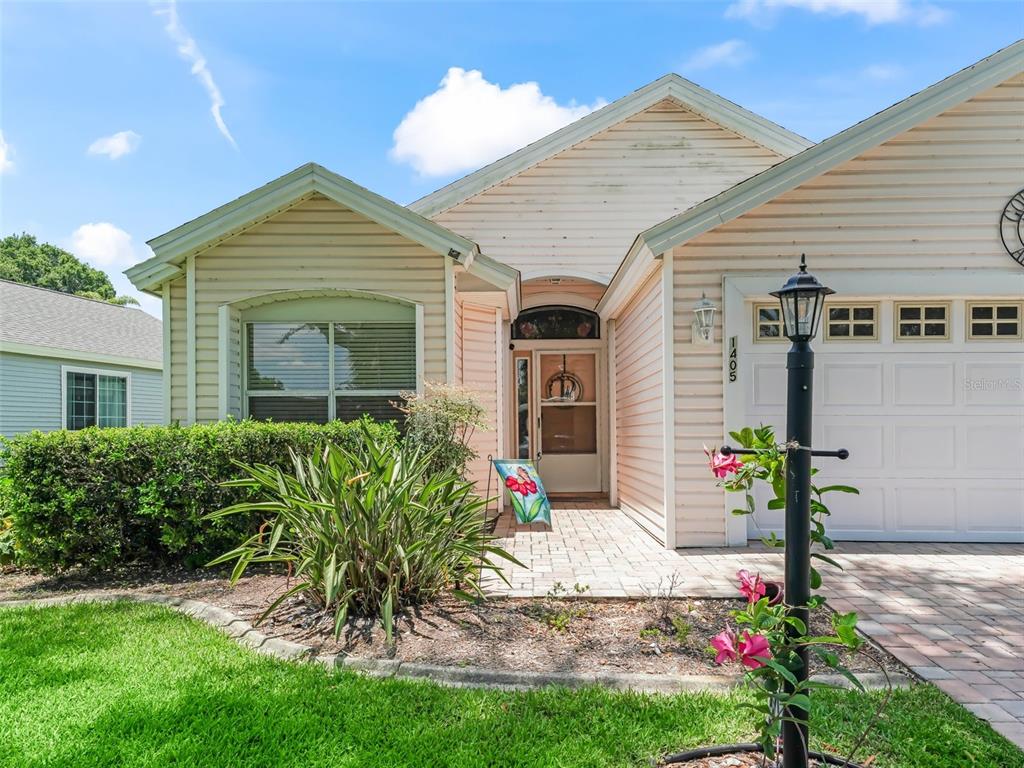 A single-story house with light-colored siding, a paved walkway, and a front-facing garage — 1405 W SCHWARTZ BOULEVARD, THE VILLAGES, FL