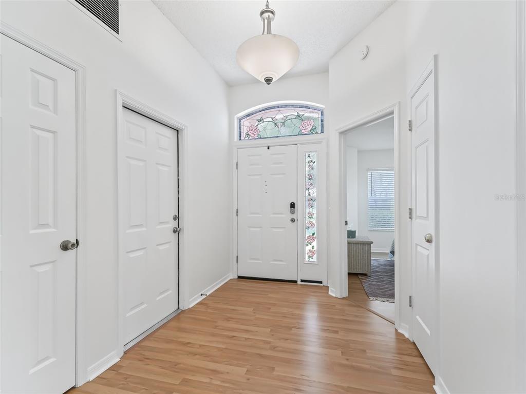 A bright entryway features wood-look flooring, white doors, and a decorative stained-glass transom window — 1405 W SCHWARTZ BOULEVARD, THE VILLAGES, FL
