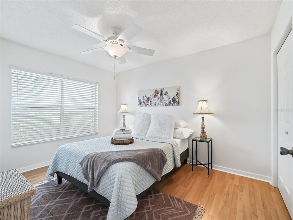 A bedroom features a bed with a light blue quilt, a ceiling fan, and wood flooring — 1405 W SCHWARTZ BOULEVARD, THE VILLAGES, FL