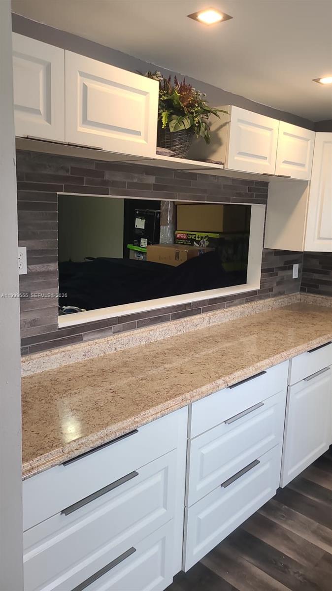 A kitchen features white cabinets, a granite countertop, and a dark tile backsplash with a cutout — 1402 NW 80th Ave # 205, Margate FL 33063, MARGATE, FL