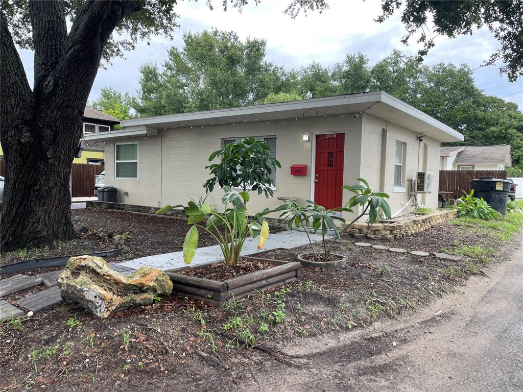 A single-story house with a red front door, concrete block walls, and a large tree — 2829 21ST STREET N, ST PETERSBURG, FL