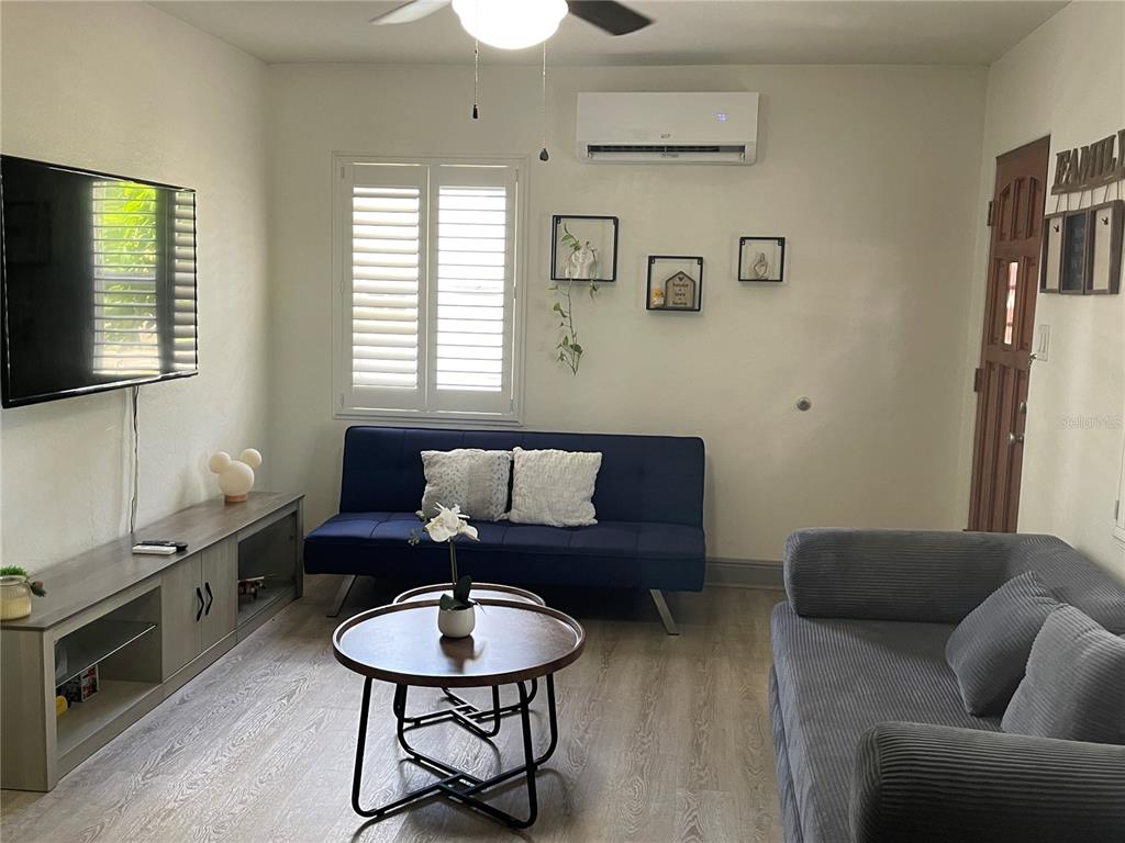 A living room features a blue futon, a grey sofa, a television, and wood-look flooring — 2829 21ST STREET N, ST PETERSBURG, FL