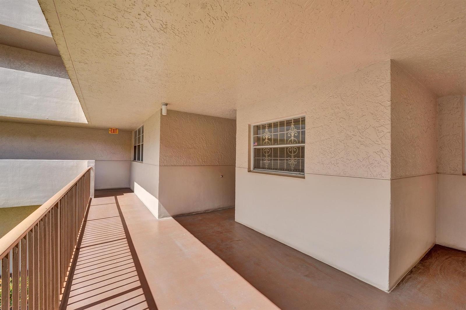 An outdoor apartment building walkway with a metal railing, a window with security bars, and stucco walls — 1811 Sabal Palm Drive # 203, Davie FL 33324, DAVIE, FL