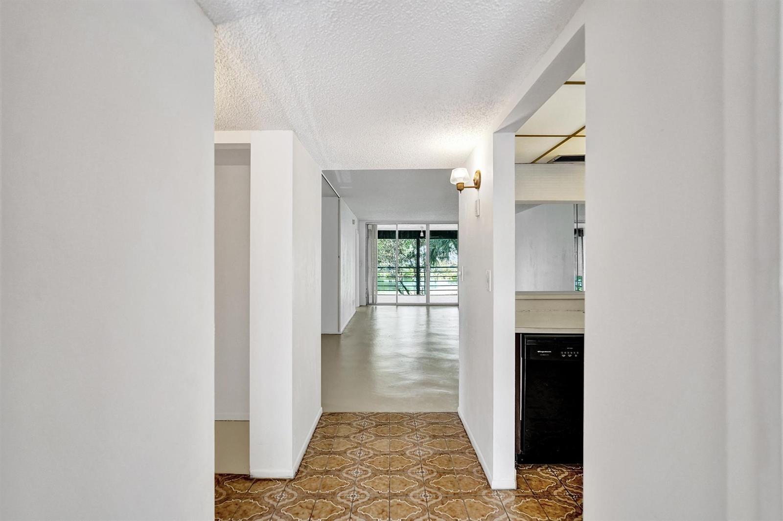 A hallway with patterned tile flooring leads toward a living area with sliding glass doors — 1811 Sabal Palm Drive # 203, Davie FL 33324, DAVIE, FL