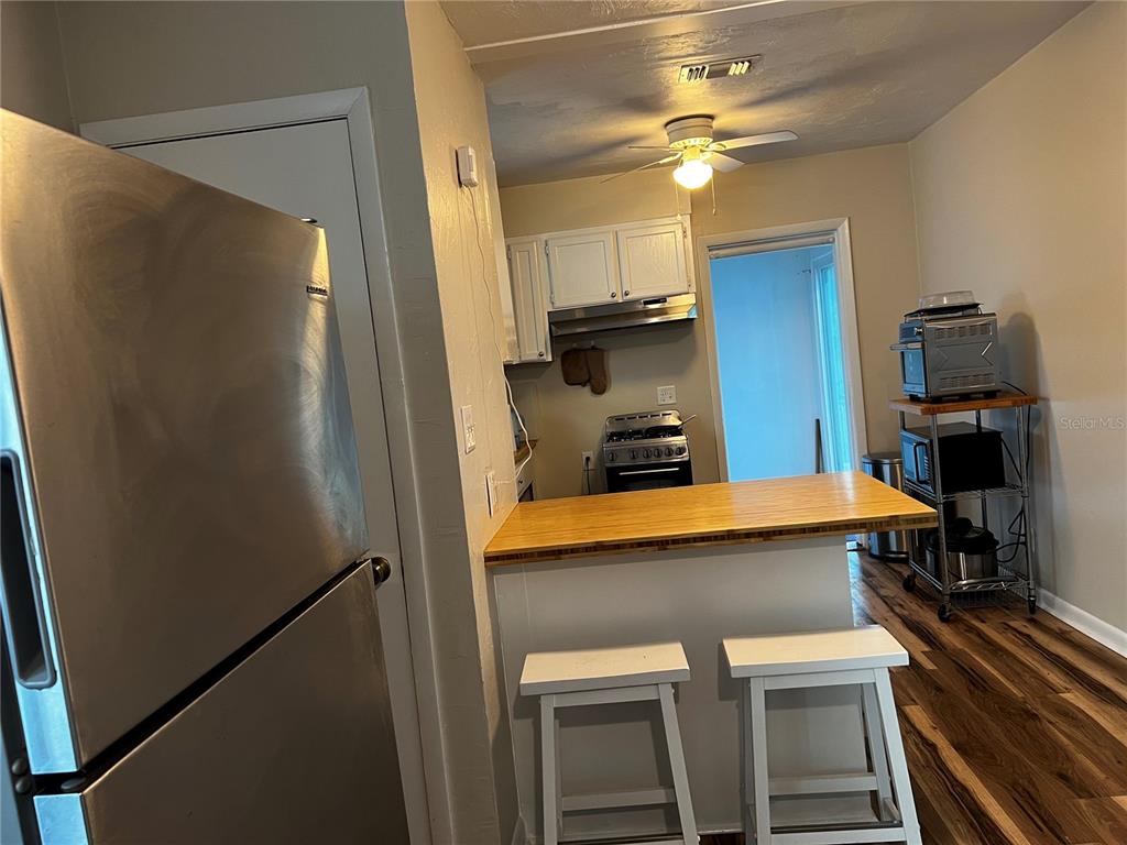 A kitchen features a stainless steel refrigerator, a wooden breakfast bar, and white cabinetry — 408 NE 18 STREET, GAINESVILLE, FL
