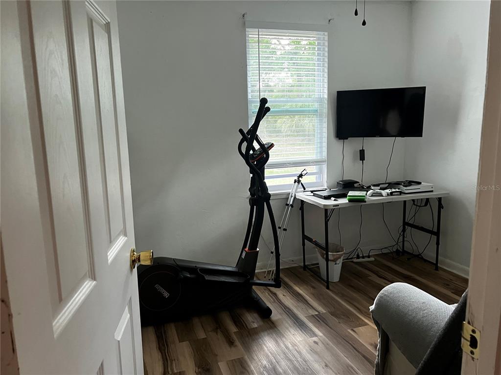 A room with wood-look flooring contains an elliptical machine, a folding table, and a television — 408 NE 18 STREET, GAINESVILLE, FL