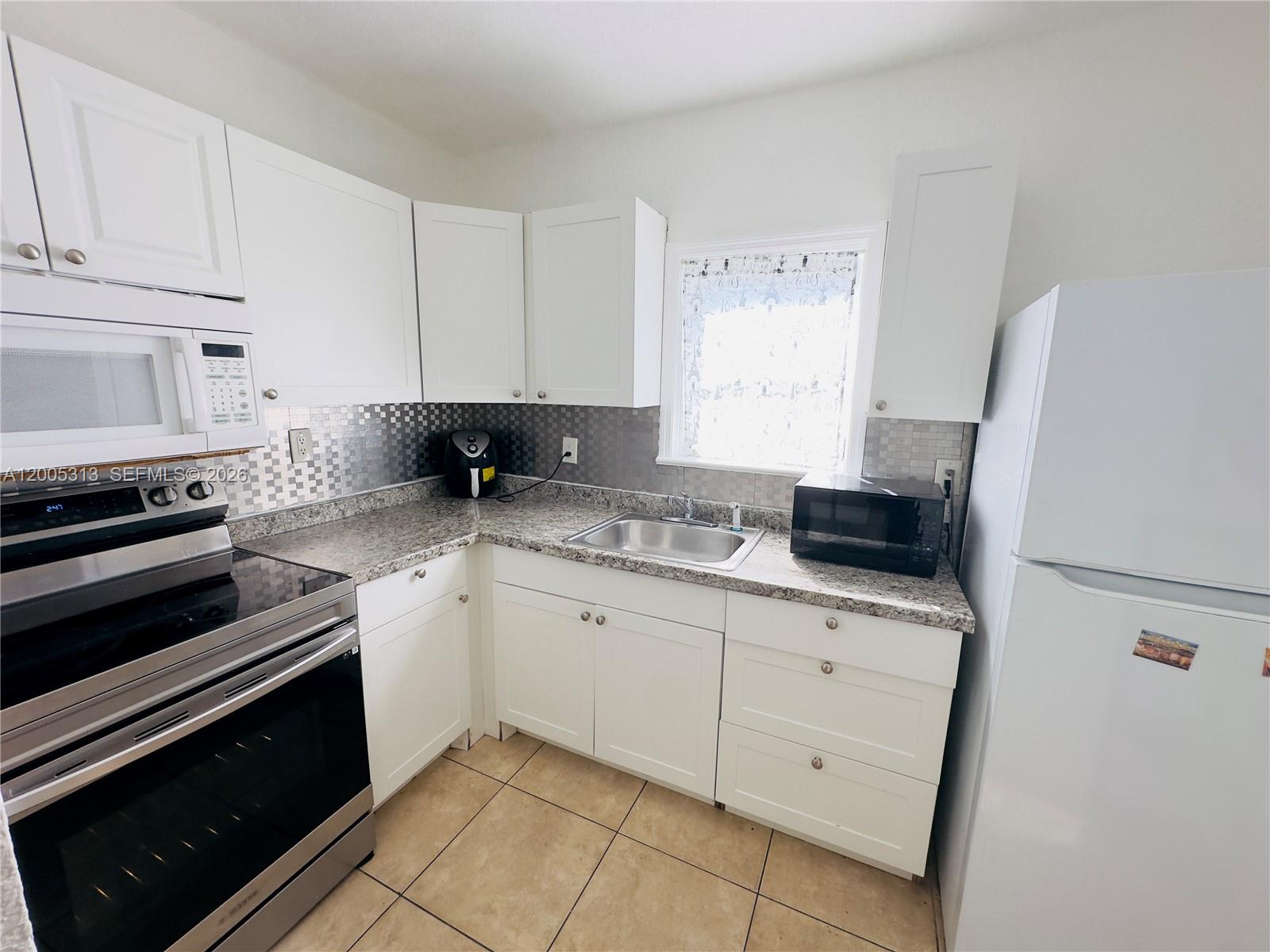 A kitchen features white cabinets, stainless steel appliances, granite countertops, and a tiled backsplash — 301 NW 37th St, Miami FL 33127, MIAMI, FL