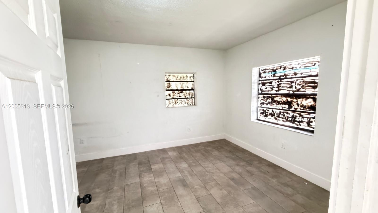 An empty room features white walls, gray tile flooring, and two glass block windows — 301 NW 37th St, Miami FL 33127, MIAMI, FL