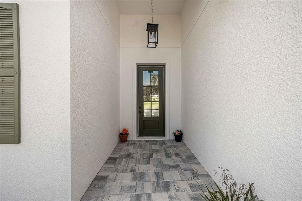 A covered entryway features a dark green door, a hanging lantern, and gray paver flooring — 4816 N CRESTLINE DRIVE, BEVERLY HILLS, FL