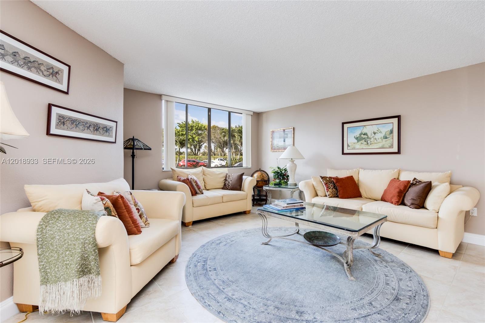 A living room features three cream-colored sofas, a glass coffee table, and a round rug — 1410 Sheridan St # 9I, Hollywood FL 33020, HOLLYWOOD, FL
