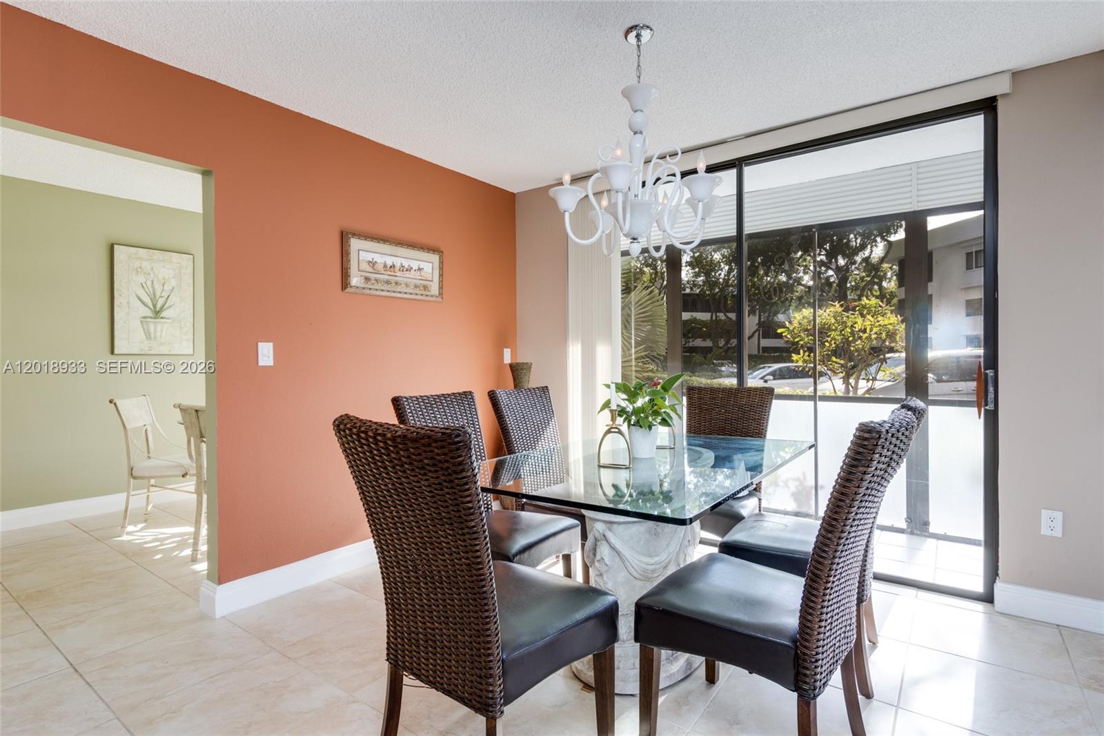 A dining room features a glass-topped table, wicker chairs, a chandelier, and sliding glass doors — 1410 Sheridan St # 9I, Hollywood FL 33020, HOLLYWOOD, FL