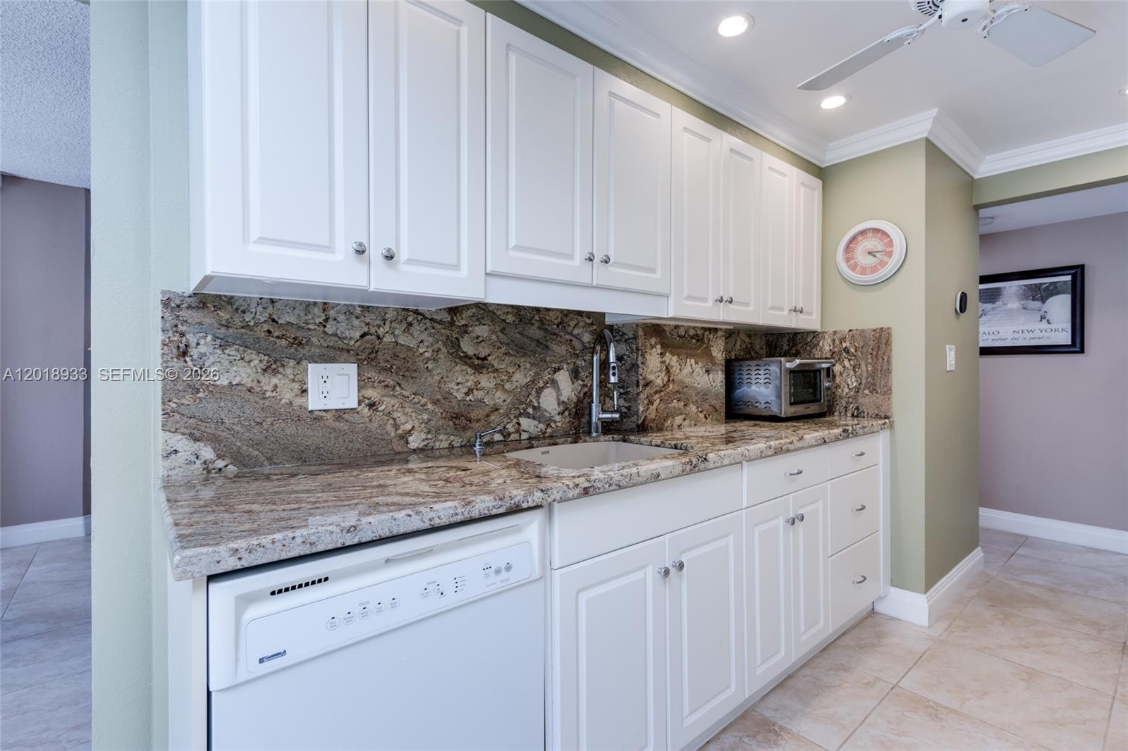 A kitchen features white cabinets, granite countertops, a stone backsplash, and a stainless steel sink — 1410 Sheridan St # 9I, Hollywood FL 33020, HOLLYWOOD, FL