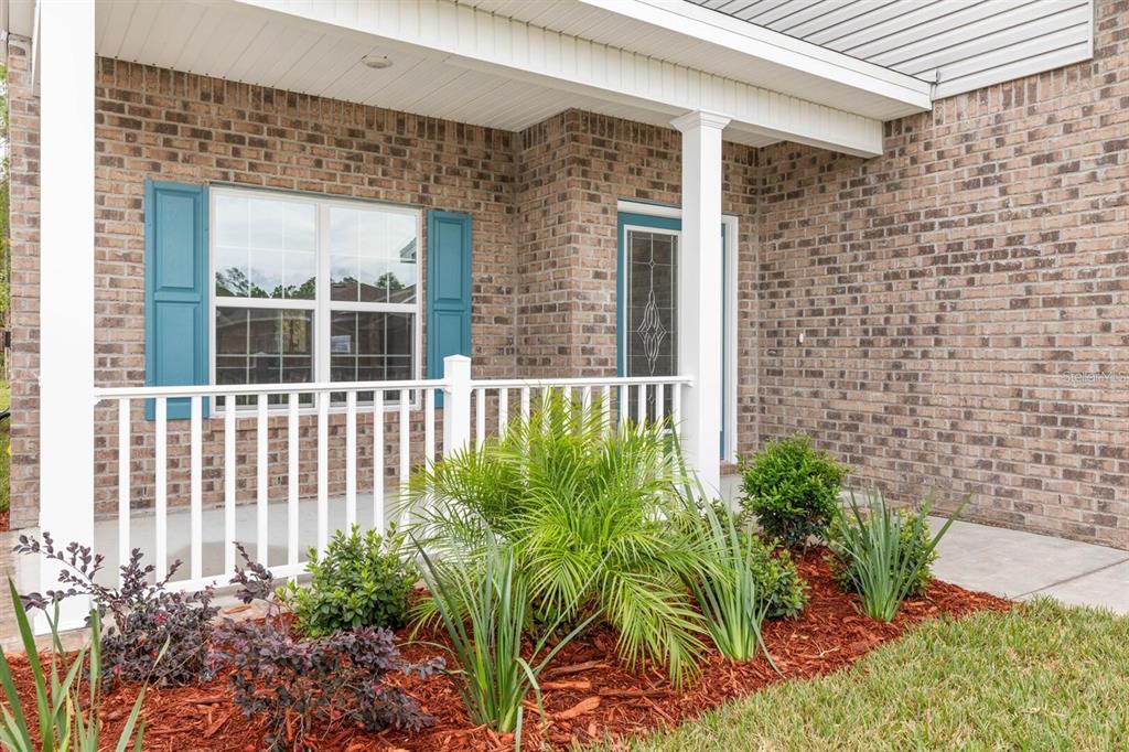A brick house exterior features a covered front porch with white railings and blue shutters — 18 RENMONT PLACE, PALM COAST, FL