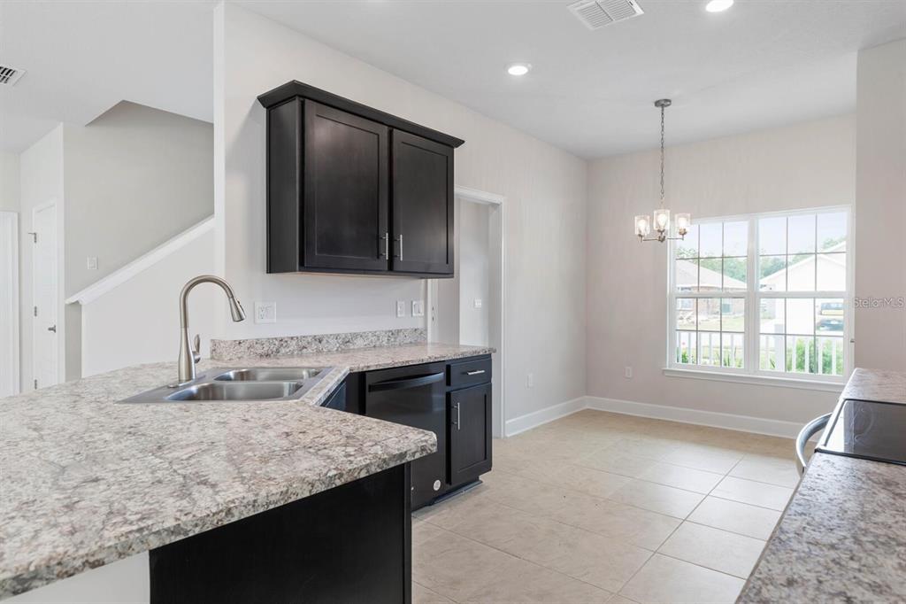 A kitchen with dark cabinets, granite countertops, and an adjacent dining area with a chandelier — 18 RENMONT PLACE, PALM COAST, FL
