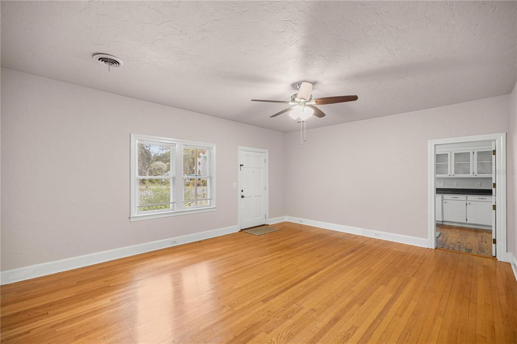 An empty living room features hardwood floors, a ceiling fan, and a doorway to the kitchen — 5915 AVENUE F, MC INTOSH, FL
