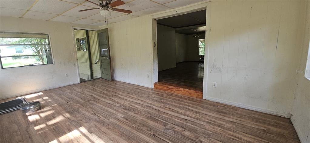 An interior view shows a room with wood-look flooring, white paneled walls, and a ceiling fan — 107 APACHE AVENUE, INTERLACHEN, FL
