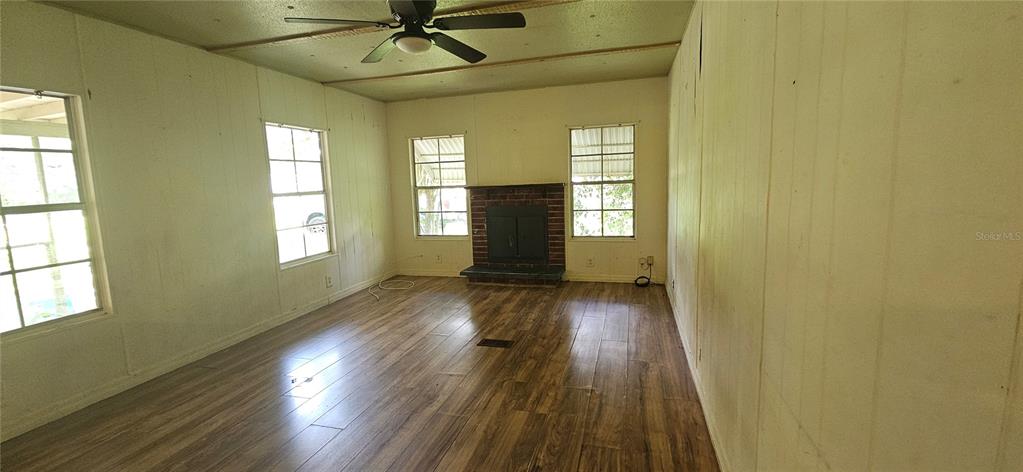 A living room features wood-look flooring, white paneled walls, a ceiling fan, and a fireplace — 107 APACHE AVENUE, INTERLACHEN, FL