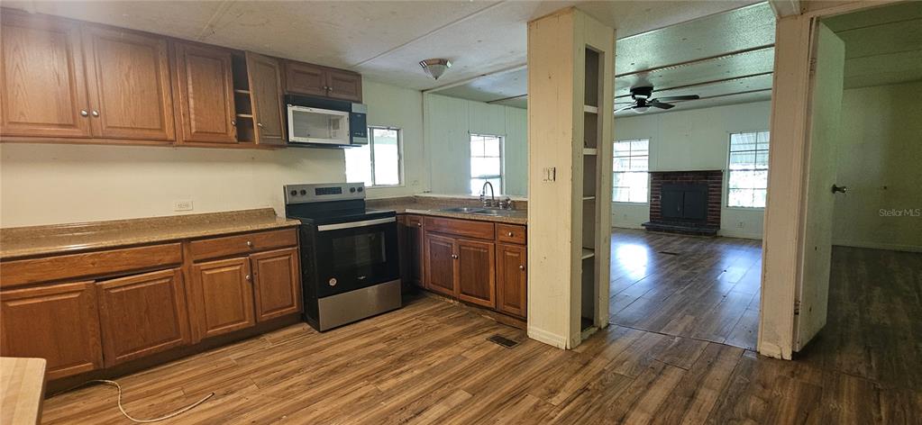 A kitchen with wood cabinets and a stainless steel stove opens into a living area — 107 APACHE AVENUE, INTERLACHEN, FL